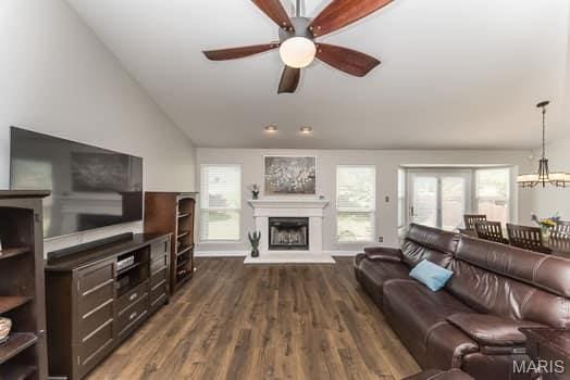 1405 Sunburst Dr, O'Fallon, MO 63366 - living room featuring ceiling fan, a fireplace with raised hearth, vaulted ceiling, dark wood-type flooring, and a chandelier