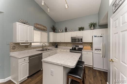 1405 Sunburst Dr, O'Fallon, MO 63366 - kitchen with stainless steel appliances, vaulted ceiling, dark wood finished floors, tasteful backsplash, and white cabinetry