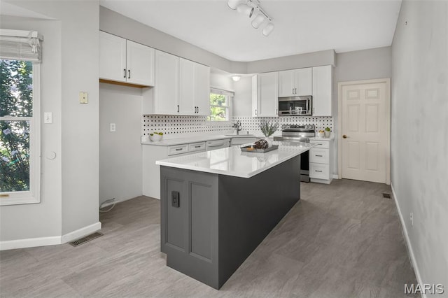2849 Dardenne Links Dr, Dardenne Prairie, MO 63368 - kitchen featuring stainless steel appliances, decorative backsplash, white cabinets, light countertops, and a kitchen island