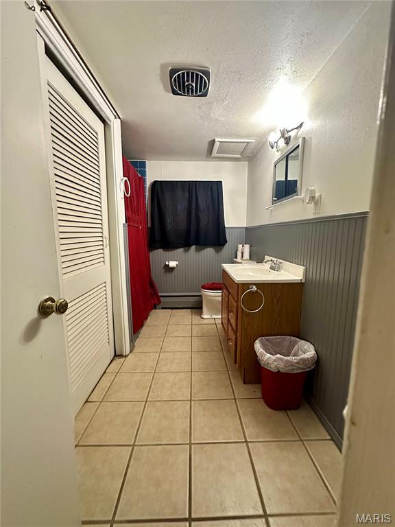 918 E 7th St, Rolla, MO 65401 - full bathroom featuring a baseboard radiator, vanity, wainscoting, tile patterned floors, and a textured ceiling