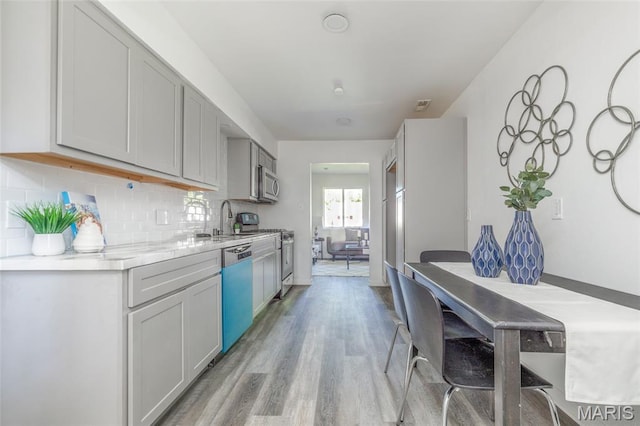10141 Ventura Dr, Ferguson Township, MO 63136 - kitchen featuring dishwasher, gas range, light wood-style flooring, light countertops, and backsplash