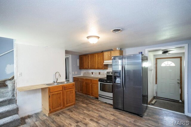 200 S Frisco, Crocker, MO 65452 - kitchen with appliances with stainless steel finishes, under cabinet range hood, dark wood-style floors, a textured ceiling, and brown cabinetry