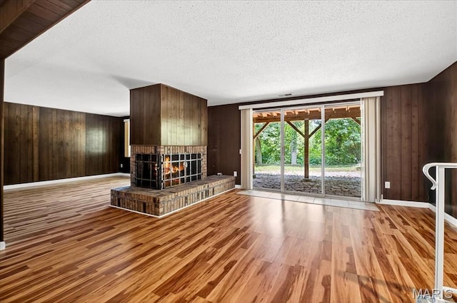775 Knickerbacker Dr, Manchester, MO 63021 - unfurnished living room with wood finished floors, wooden walls, a brick fireplace, and a textured ceiling