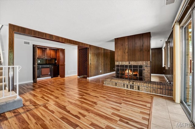 775 Knickerbacker Dr, Manchester, MO 63021 - unfurnished living room with a fireplace, wood walls, light wood-style floors, plenty of natural light, and a textured ceiling