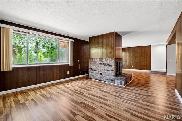 775 Knickerbacker Dr, Manchester, MO 63021 - unfurnished living room with light wood-style flooring, wooden walls, a textured ceiling, and a fireplace