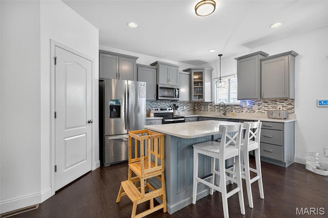 231 Flint Brook Dr, Ofallon, MO 63366 - kitchen with appliances with stainless steel finishes, gray cabinets, a breakfast bar area, tasteful backsplash, and recessed lighting