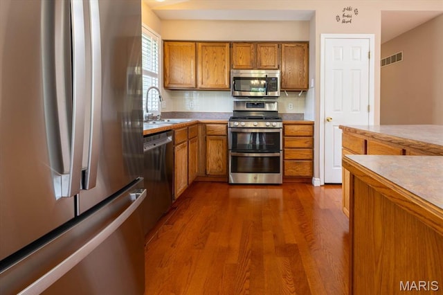 1715 Foxglove Dr, Saint Charles, MO 63303 - kitchen with appliances with stainless steel finishes, brown cabinets, dark wood-style floors, tasteful backsplash, and light countertops