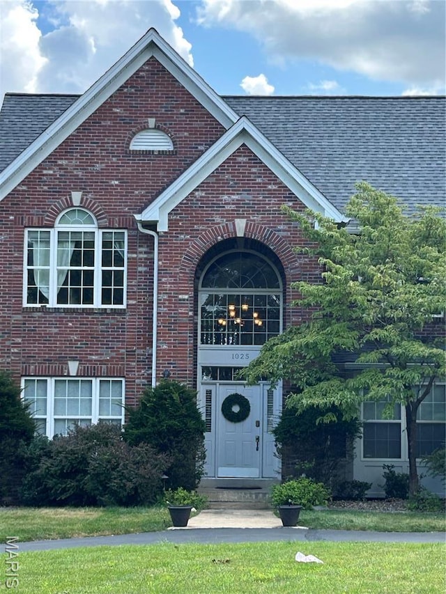 view of exterior entry featuring brick siding, roof with shingles, and a yard
