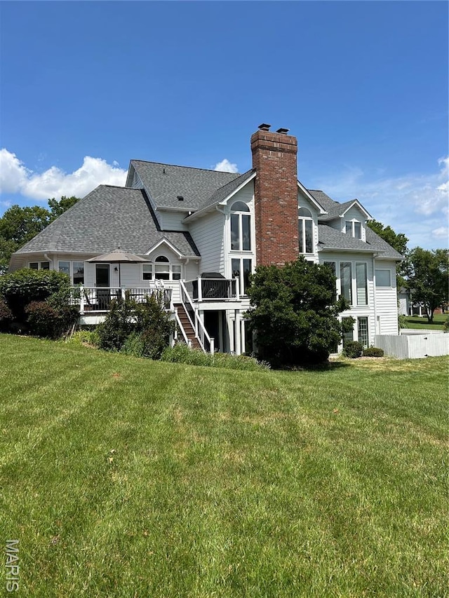 back of house featuring a chimney, a yard, a deck, and roof with shingles