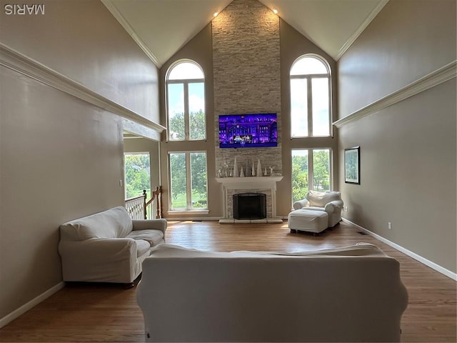 living area featuring high vaulted ceiling, healthy amount of natural light, a fireplace, ornamental molding, and wood finished floors