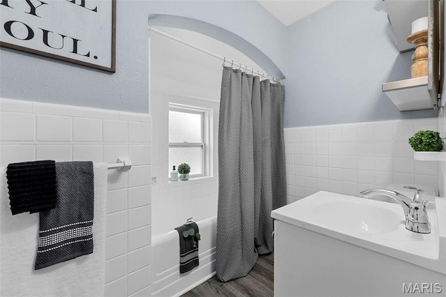 6629 Barken Ave, Northwoods, MO 63121 - bathroom with tile walls, shower / bath combo with shower curtain, wood finished floors, a wainscoted wall, and vanity