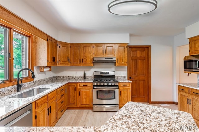 616 E Brentmoor Dr, Troy, IL 62294 - kitchen featuring appliances with stainless steel finishes, under cabinet range hood, light stone counters, brown cabinetry, and light wood-type flooring