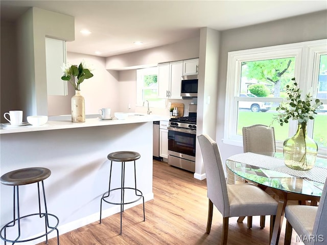 1248 Lynchester Ln, Kirkwood, MO 63122 - kitchen featuring appliances with stainless steel finishes, a breakfast bar area, white cabinetry, light wood-style flooring, and light countertops