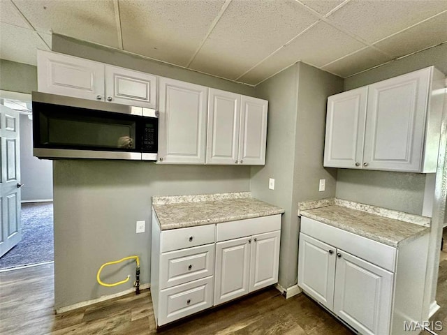 316 Church St, East Alton, IL 62024 - kitchen featuring stainless steel microwave, a paneled ceiling, white cabinetry, dark wood-style flooring, and light countertops