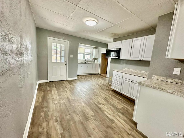 316 Church St, East Alton, IL 62024 - kitchen featuring stainless steel microwave, a drop ceiling, white cabinetry, light wood-style flooring, and a textured wall