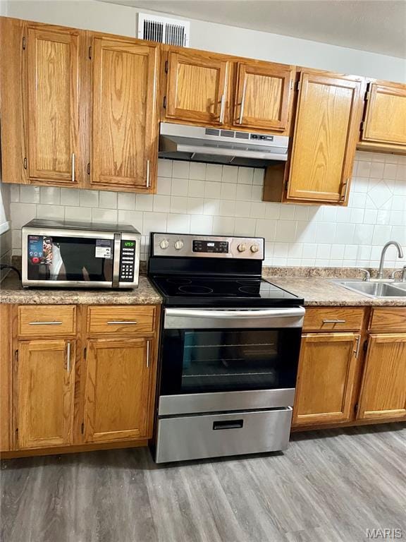 9264 Bellefontaine Rd, Bellefontaine Nghbrs, MO 63137 - kitchen featuring appliances with stainless steel finishes, under cabinet range hood, light wood-style flooring, and tasteful backsplash