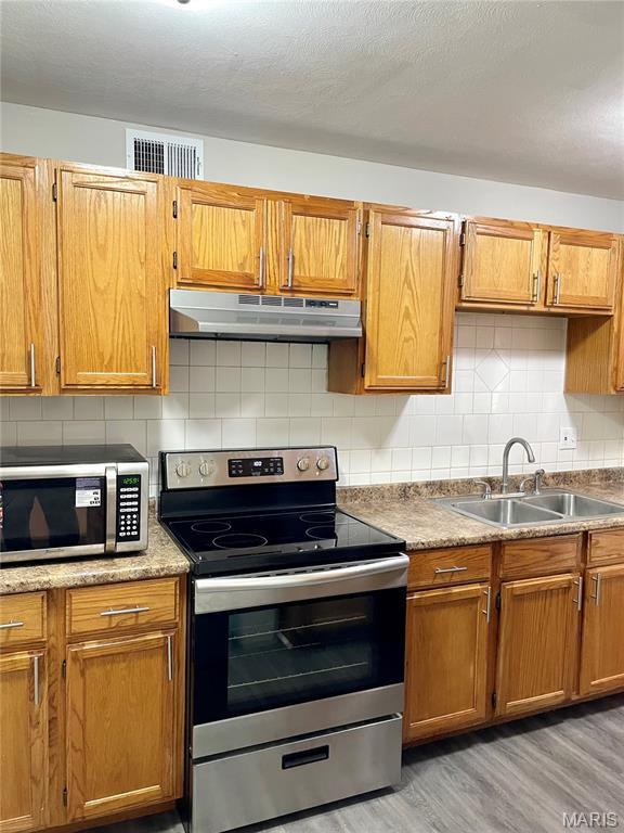 9264 Bellefontaine Rd, Bellefontaine Nghbrs, MO 63137 - kitchen with stainless steel appliances, under cabinet range hood, light wood-type flooring, and decorative backsplash