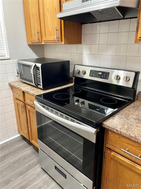 9264 Bellefontaine Rd, Bellefontaine Nghbrs, MO 63137 - kitchen with stainless steel appliances, range hood, light wood-style flooring, tile walls, and brown cabinets