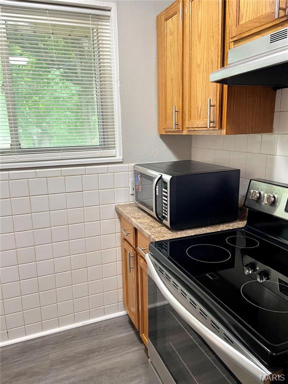 9264 Bellefontaine Rd, Bellefontaine Nghbrs, MO 63137 - kitchen with electric stove, under cabinet range hood, black microwave, tile walls, and wood finished floors