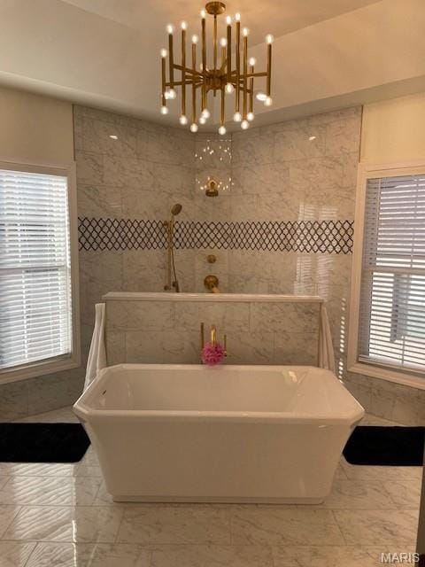 8145 University Dr, Clayton, MO 63105 - bathroom featuring a soaking tub, a chandelier, marble look tiles, and tile walls