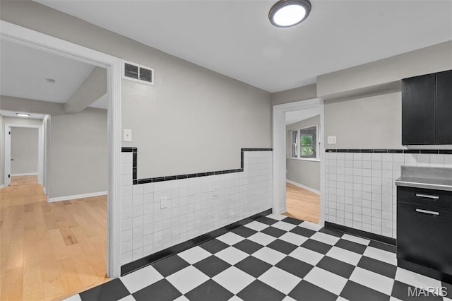 7315 Ahern Ave, University City, MO 63130 - kitchen with tile walls, dark cabinetry, a wainscoted wall, light countertops, and light flooring