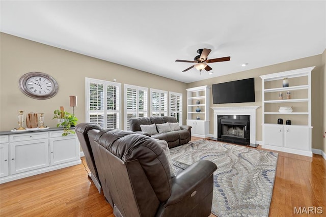 1304 Forest Way, Wentzville, MO 63385 - living room featuring ceiling fan, light wood finished floors, a fireplace with raised hearth, and built in shelves