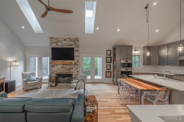 2740 Tyrol View Ct, Innsbrook, MO 63390 - living room featuring a skylight, ceiling fan, high vaulted ceiling, a stone fireplace, and light wood finished floors