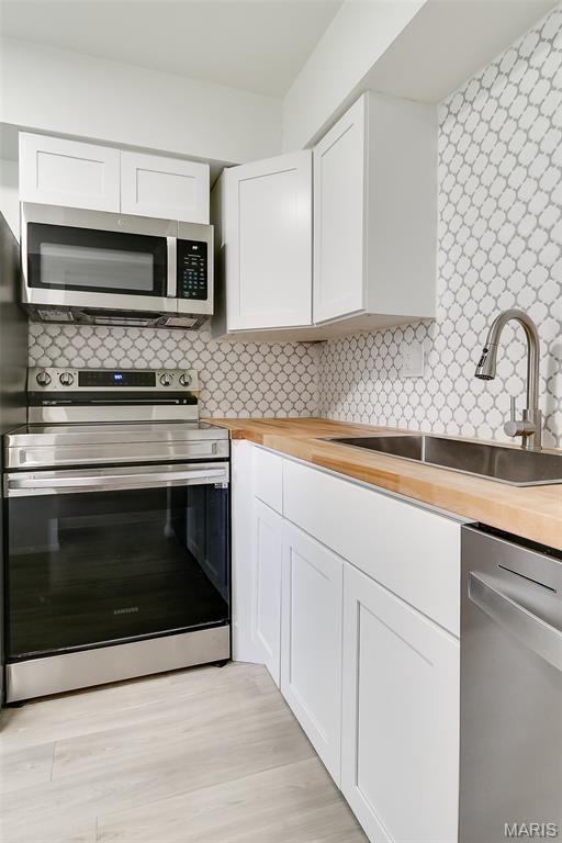 8733 Sieloff Dr Unit C, Hazelwood, MO 63042 - kitchen featuring butcher block countertops, appliances with stainless steel finishes, white cabinets, tasteful backsplash, and light wood-style flooring