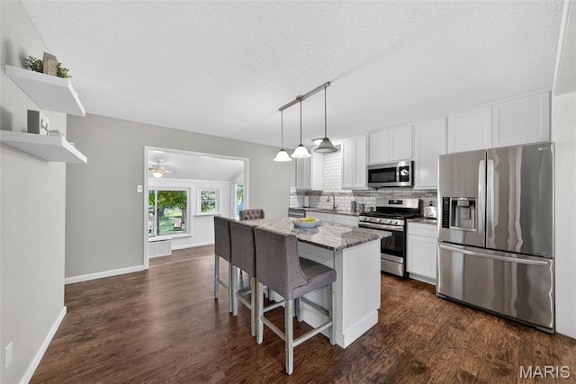 1002 Arlington Dr, Saint Charles, MO 63303 - kitchen featuring appliances with stainless steel finishes, a textured ceiling, a kitchen island, a kitchen bar, and open shelves