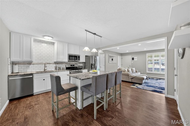 1002 Arlington Dr, Saint Charles, MO 63303 - kitchen featuring appliances with stainless steel finishes, dark wood-type flooring, a kitchen breakfast bar, a textured ceiling, and a kitchen island