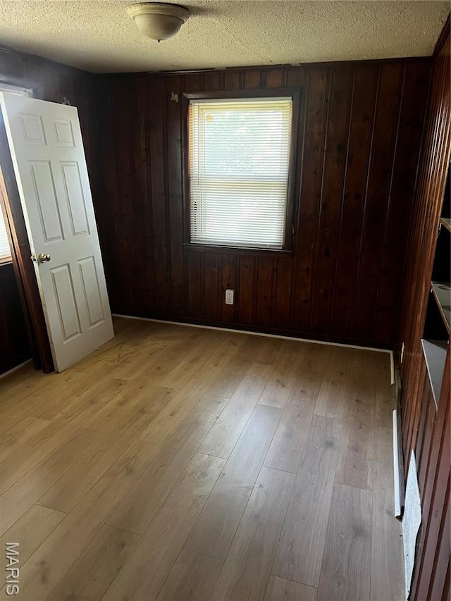 5209 College Ave, Jennings, MO 63136 - unfurnished bedroom featuring a textured ceiling, light wood-style floors, and wood walls