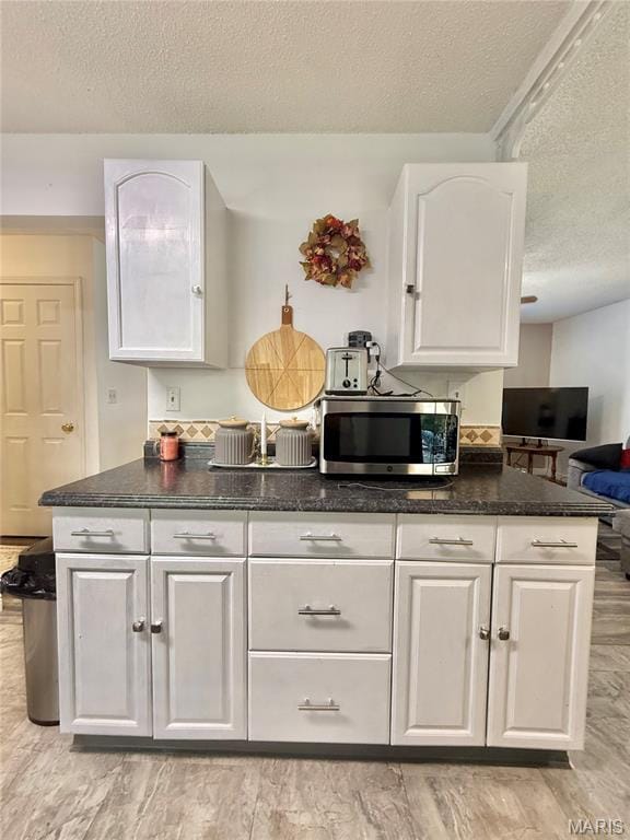 2284 Sunnyridge Dr, Arnold, MO 63010 - kitchen with stainless steel microwave, a textured ceiling, white cabinets, dark stone counters, and light wood finished floors