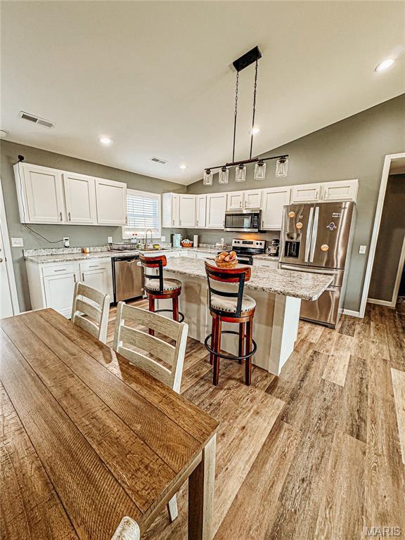 9 Powers Ln, Sikeston, MO 63801 - kitchen featuring appliances with stainless steel finishes, white cabinetry, light wood-type flooring, a kitchen island, and light stone counters