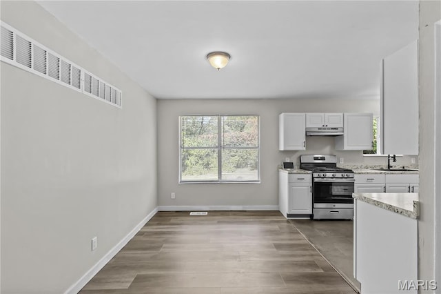 10411 Royal Dr, Saint Louis, MO 63136 - kitchen with gas range, white cabinetry, under cabinet range hood, and wood finished floors