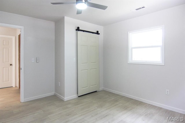 320 E Davidson Ave, Chaffee, MO 63740 - unfurnished bedroom featuring a barn door, light wood finished floors, and ceiling fan
