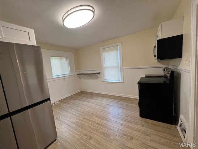 5502 Helen Ave, Saint Louis, MO 63136 - kitchen with freestanding refrigerator, white cabinetry, stove, light wood-type flooring, and a wainscoted wall
