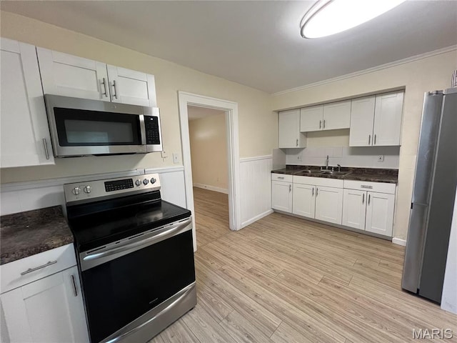 5502 Helen Ave, Saint Louis, MO 63136 - kitchen with stainless steel appliances, light wood-style floors, dark countertops, wainscoting, and white cabinets
