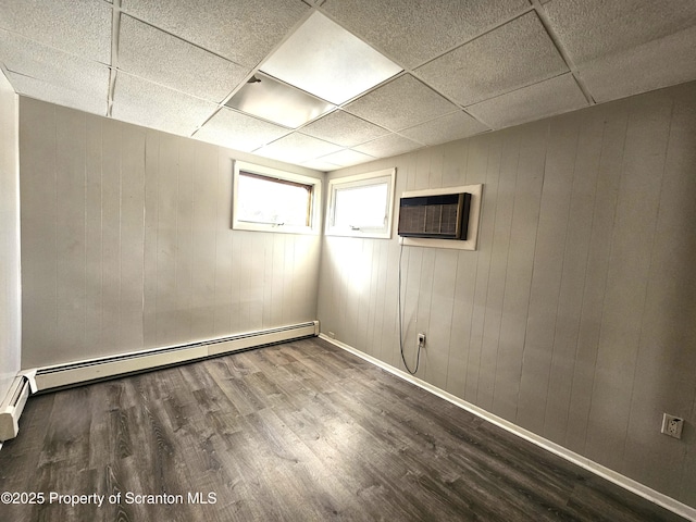 basement with wood-type flooring, a wall unit AC, a drop ceiling, and baseboard heating