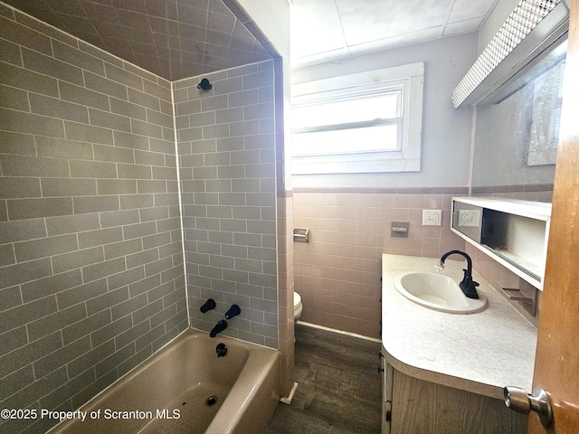 full bathroom featuring vanity, toilet, tiled shower / bath combo, and tile walls