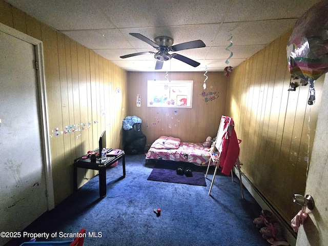 carpeted bedroom featuring ceiling fan, a paneled ceiling, wood walls, and a baseboard heating unit