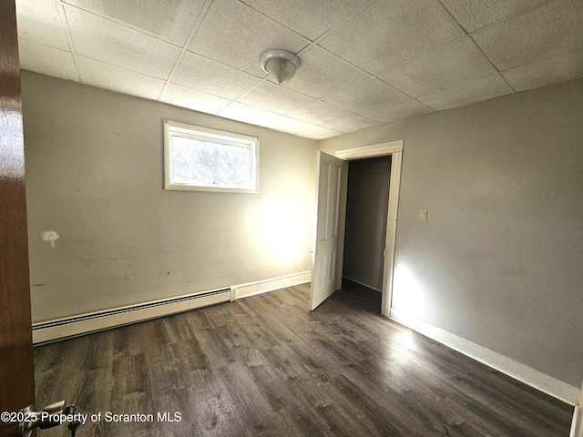 empty room with dark wood-type flooring, a drop ceiling, and a baseboard heating unit