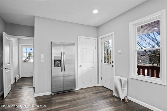 kitchen with stainless steel refrigerator with ice dispenser, a healthy amount of sunlight, radiator heating unit, and dark wood-type flooring