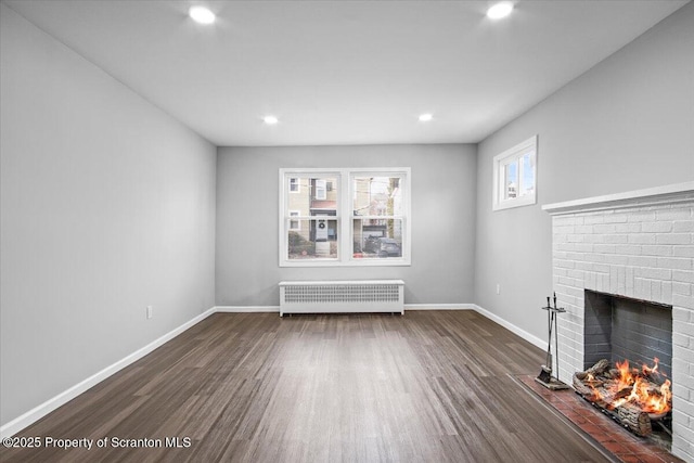 unfurnished living room featuring radiator heating unit, dark hardwood / wood-style flooring, and a brick fireplace