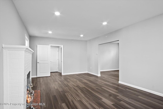 unfurnished living room featuring a brick fireplace and dark wood-type flooring