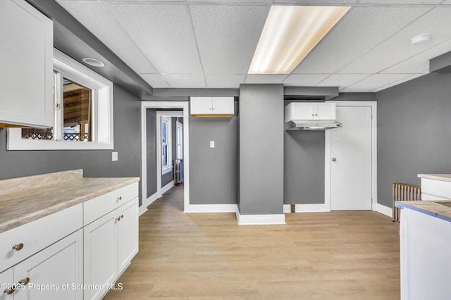 kitchen with light wood-style floors, light countertops, white cabinetry, baseboards, and a drop ceiling