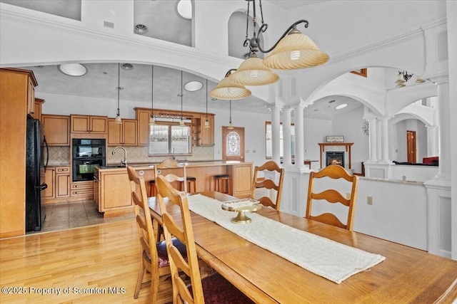 dining room featuring sink, a towering ceiling, decorative columns, and light wood-type flooring