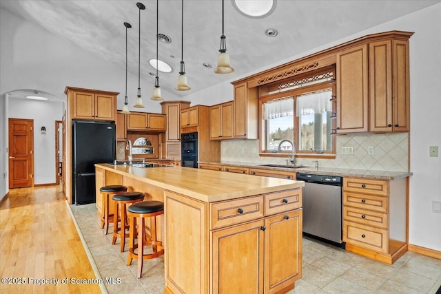 kitchen featuring pendant lighting, sink, black appliances, an island with sink, and vaulted ceiling