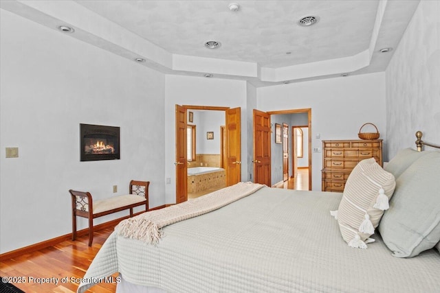 bedroom featuring connected bathroom, a tray ceiling, and wood-type flooring