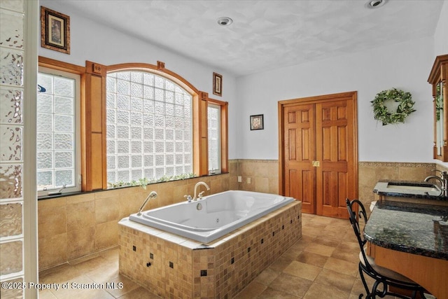 bathroom with tiled tub, sink, a healthy amount of sunlight, and tile walls