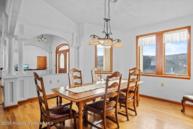 dining room with a healthy amount of sunlight, vaulted ceiling, light hardwood / wood-style flooring, and ornate columns